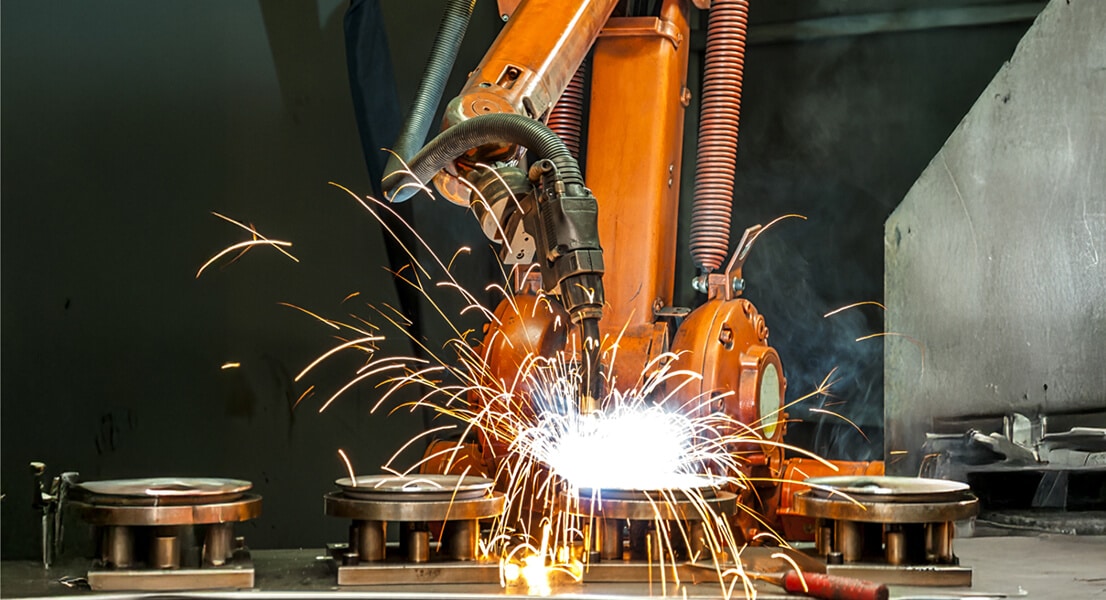 A robotic arm welding metal components on an industrial machine in a factory setting.