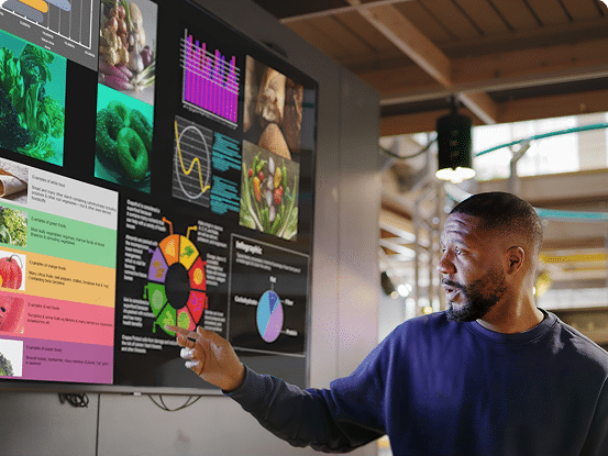 Person pointing at a large screen with charts and images about vegetables and nutrition.