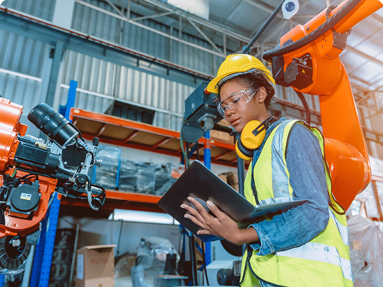 Worker in safety gear using a tablet to interact with a robotic arm in an industrial facility.