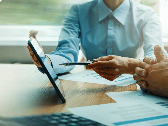 Two people reviewing charts and graphs on a tablet and documents at a table.