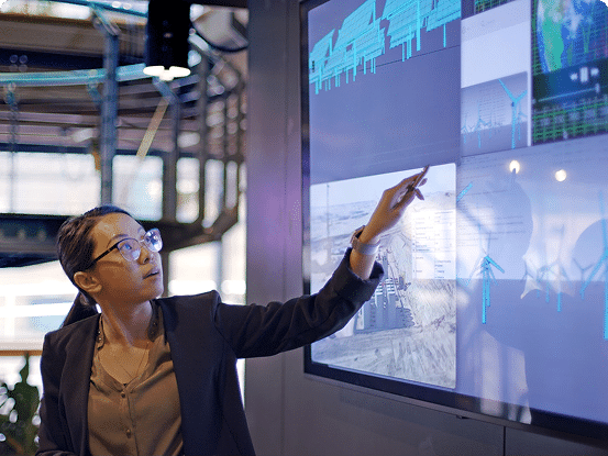 Person in business attire pointing at a screen with charts and wind turbine icons