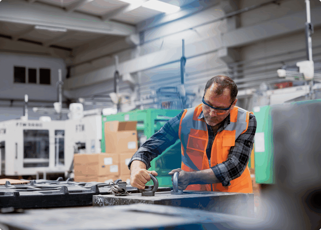 A man in an orange vest operates a machine, focused on his task in a work environment.