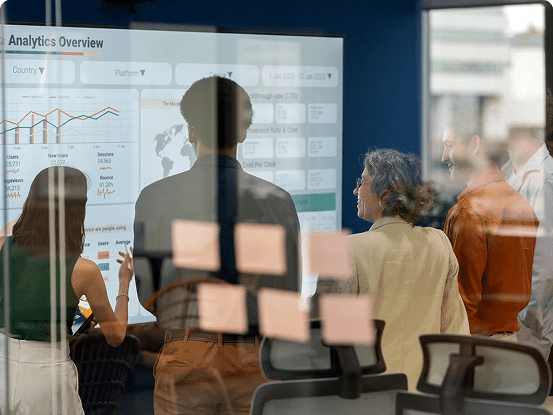 Group of people viewing a large screen with analytics charts and sticky notes on a glass wall in the foreground