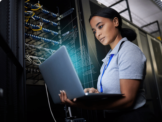 Person working on a laptop next to server racks in a server room.