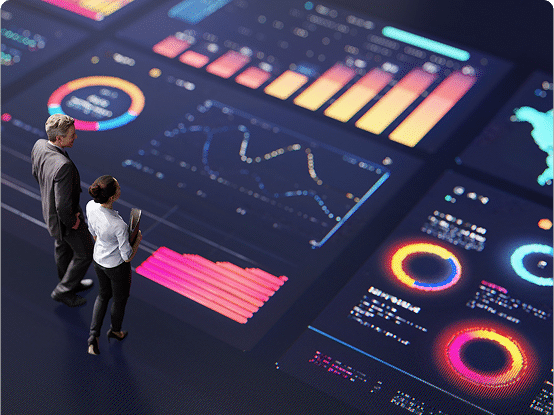 Two people stand in front of a large digital display showing colorful data visualizations, including bar charts, line graphs, and pie charts.
