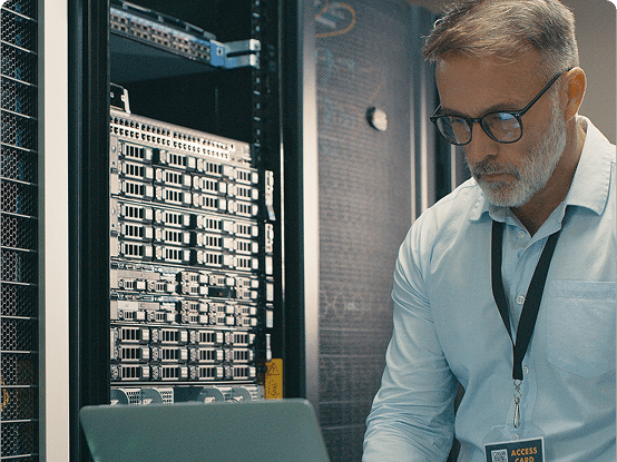 A person in a light blue shirt with an "ACCESS CARD" badge stands in front of server racks filled with network equipment in a data center.