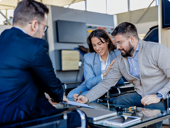 Three people sit around a glass table in an office, reviewing and discussing a document, with pens and papers scattered on the table.