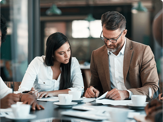 Group of people in a meeting around a table with papers, notebooks, and coffee cups