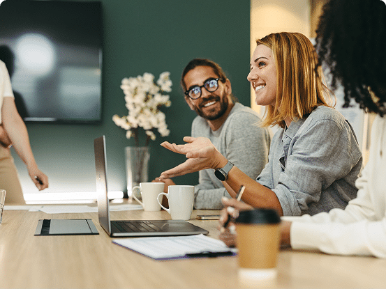 Group of people in a meeting setting with laptops, notebooks, and coffee cups on the table; faces are blurred.