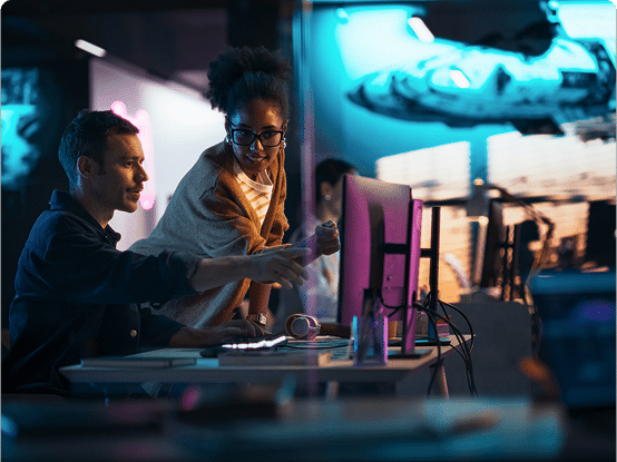 Two people working at a computer with a large screen showing a blue-lit spaceship or futuristic vehicle.