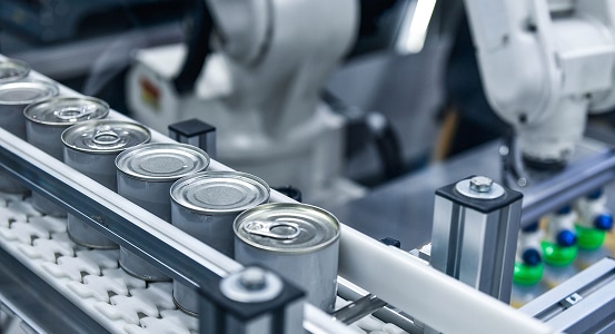 Food & Beverage Manufacturing Factory production line with metal cans on a conveyor belt and robotic arms in the background.